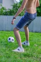 giovane in jeans denim e scarpe da ginnastica bianche che giocano a pallone da calcio all'aperto. giocatore di football amatoriale coniare la palla foto