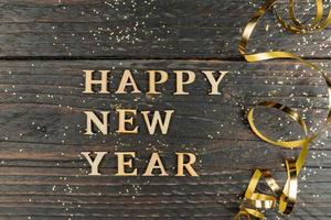 iscrizione felice anno nuovo realizzata con lettere di legno decorate serpentina dorata festiva su sfondo di legno con spazio per la copia. biglietto di auguri per la celebrazione del nuovo anno foto