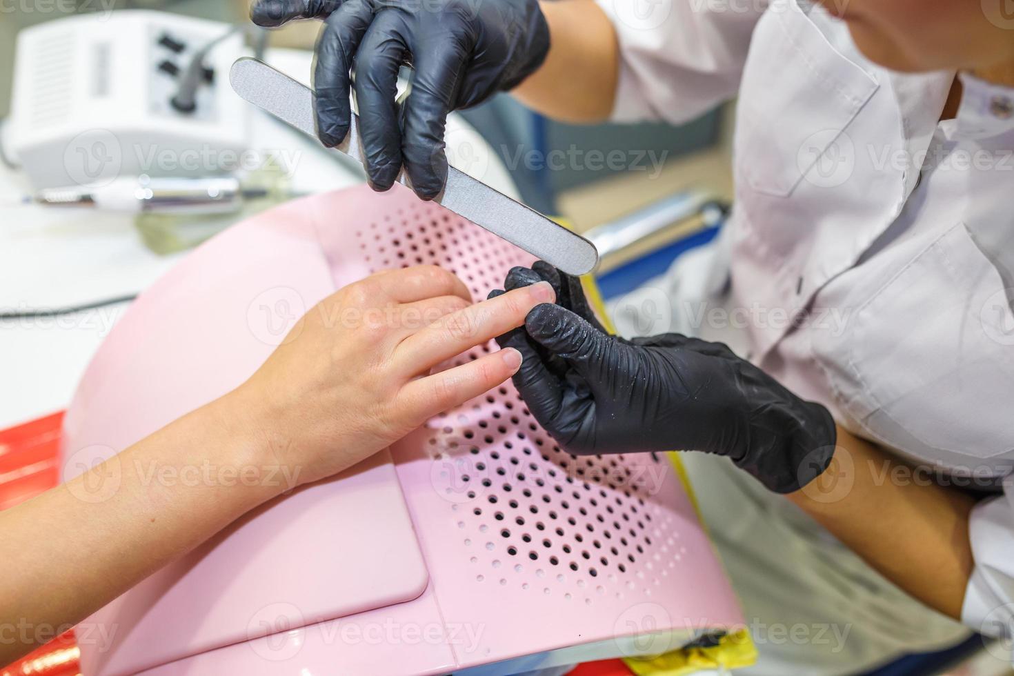 o mestre em luvas pretas no salão faz manicure pedicure para o cliente foto