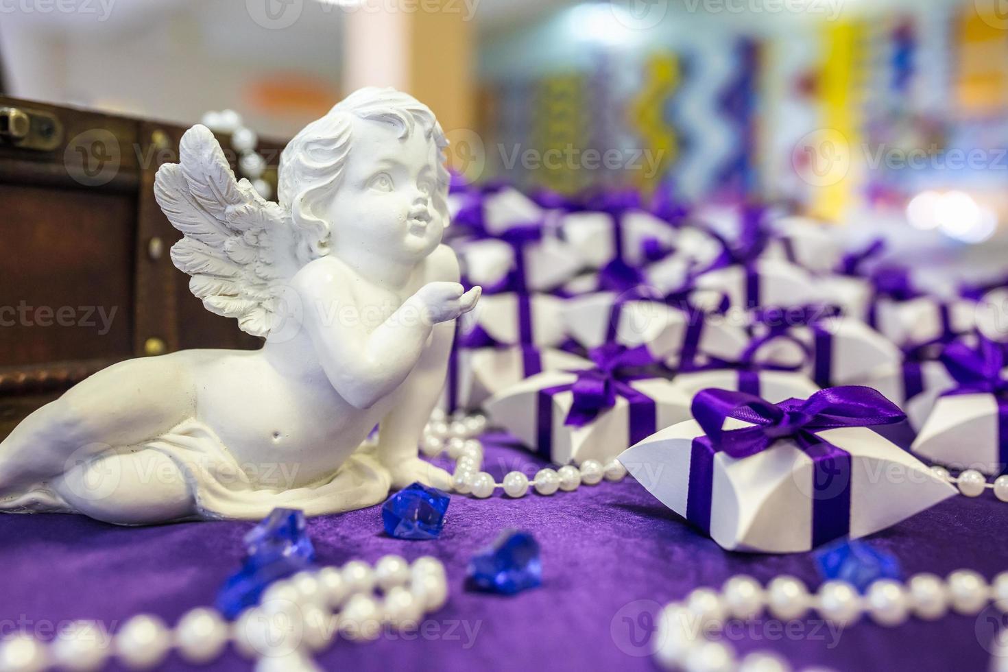 anjo de cerâmica na mesa com uma toalha de mesa violeta e pequenos presentes para convidados dos noivos foto