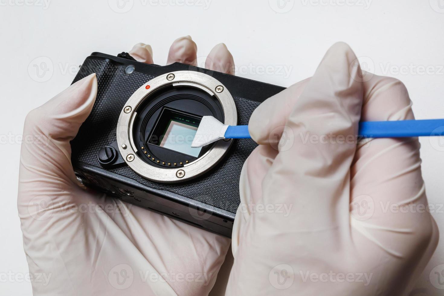 close-up da limpeza e manutenção do sensor de matriz de câmera suja digital aps-c sem espelho com cotonete, fotógrafo limpando a câmera fotográfica em fundo branco foto