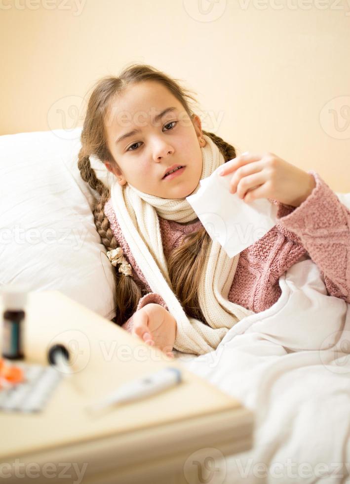 menina doente, deitada na cama e segurando o lenço de papel foto