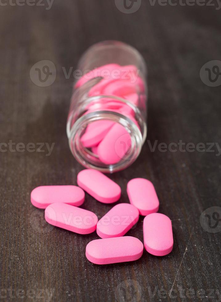 comprimidos cor de rosa, um frasco de comprimidos na mesa preta foto