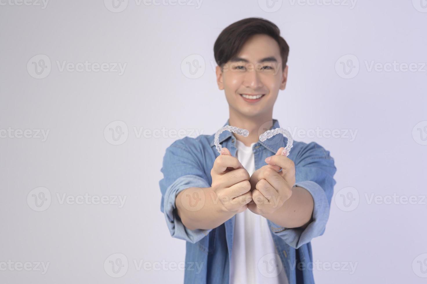 jovem sorridente segurando aparelho invisalign sobre estúdio de fundo branco, saúde bucal e conceito ortodôntico. foto