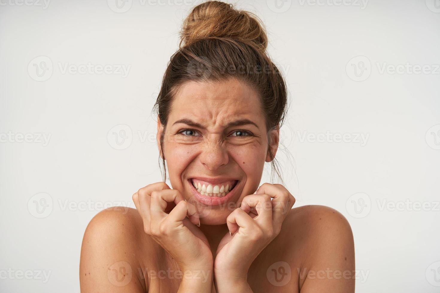 jovem mulher bonita posando sobre fundo branco com rosto assustado, com medo, segurando as mãos pelo rosto, fazendo careta e mostrando os dentes foto