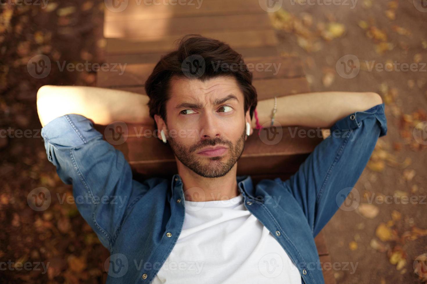 bonito jovem macho olhando de lado com cara de perplexidade, contraindo a testa e levantando as sobrancelhas foto