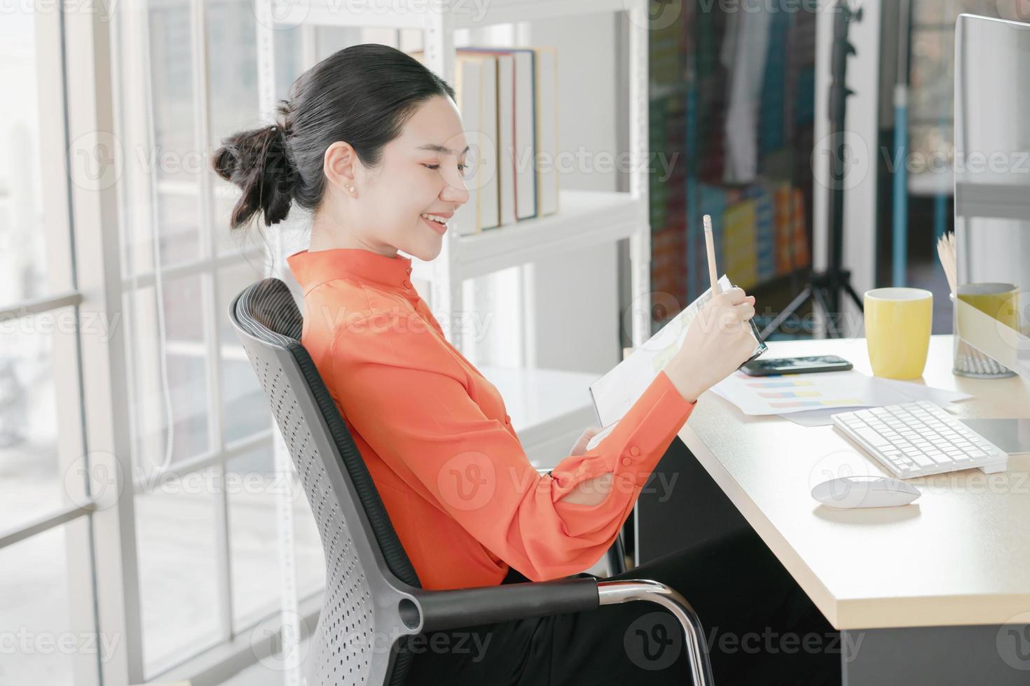empresária confiante planejando seu dia de trabalho sentado em sua mesa segurando a caneta pensando olhando para o caderno no escritório foto