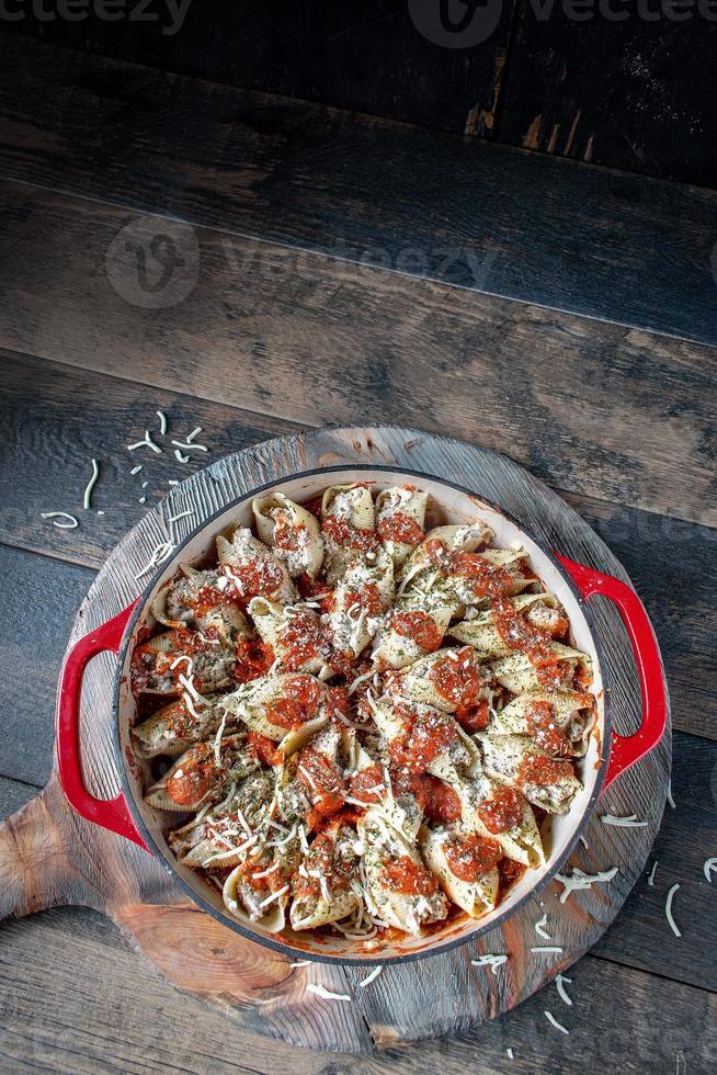 conchas de macarrão manicotti com espinafre, ricota, queijo mussarela em molho de tomate em panela vermelha em ambiente rústico configuração plana foto