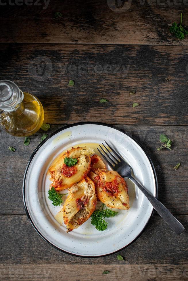 conchas de macarrão manicotti com espinafre, ricota, queijo mussarela em molho de tomate no prato em ambiente rústico configuração plana foto