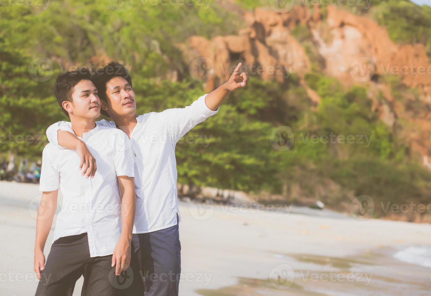 retrato homossexual jovem casal asiático em pé apontando algo juntos na praia no verão, ásia gay indo mar para lazer com romântico e feliz em férias no mar, lgbt com conceito legal. foto