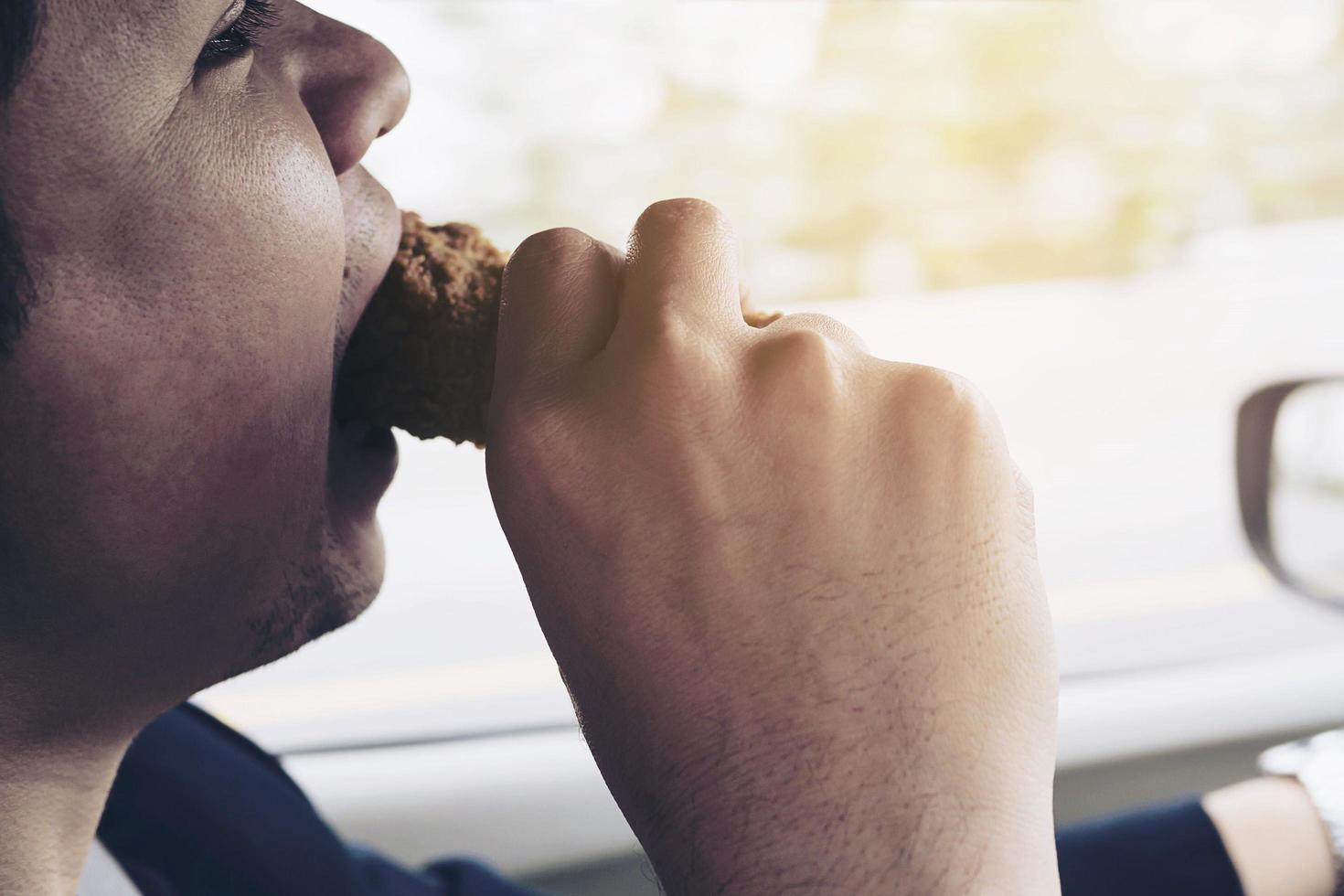 homem de negócios dirigindo carro enquanto come frango frito perigosamente foto