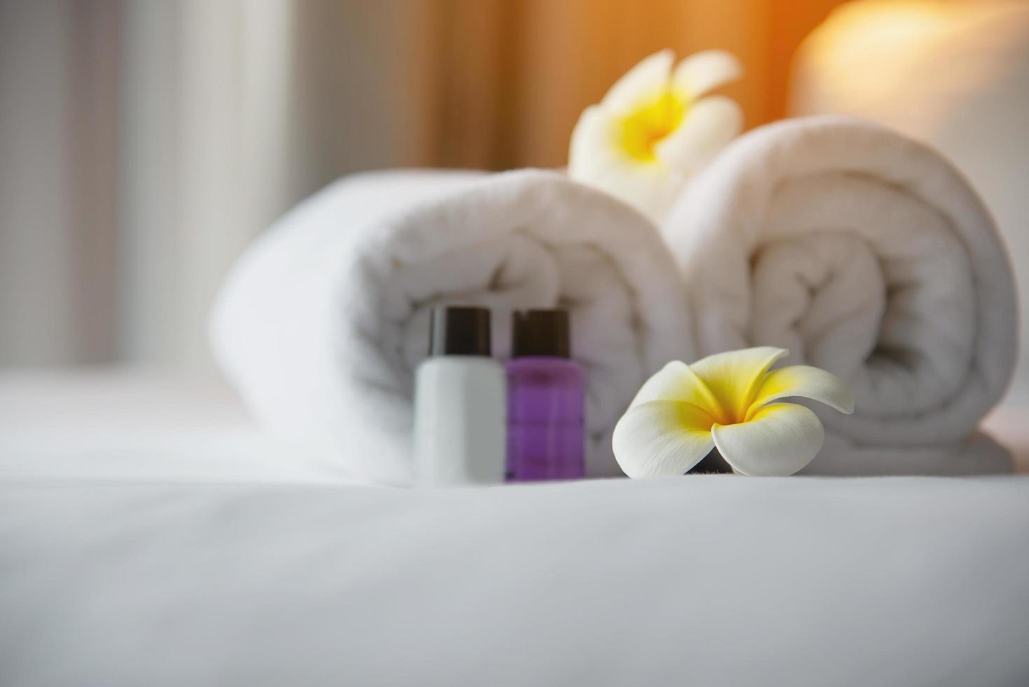 toalha de hotel e garrafa de banho de shampoo e sabonete em cama branca com flor de plumeria decorada - relaxe as férias no conceito de resort de hotel foto