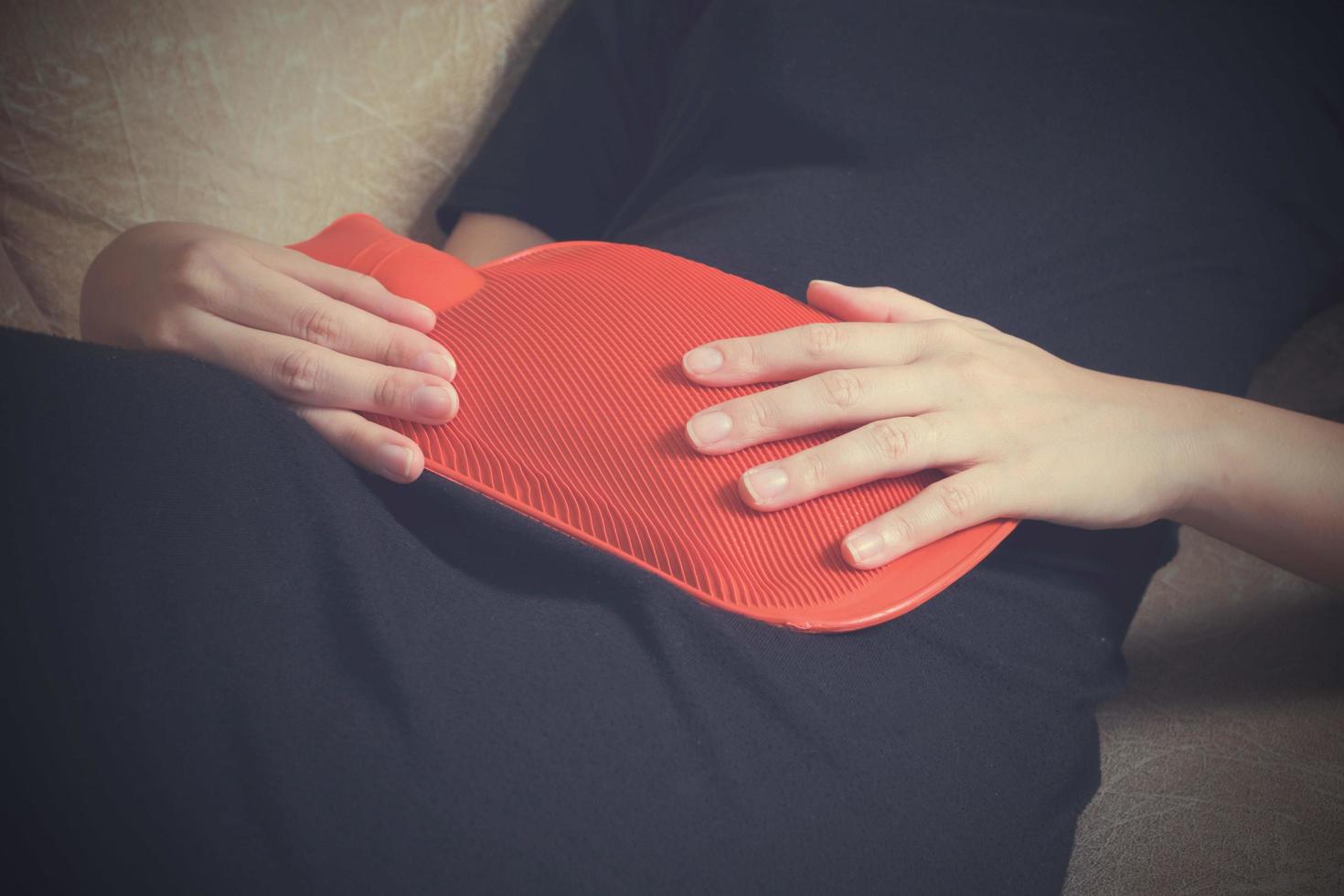 mulher doente deitada no sofá com bolsa de água quente e segurando na barriga com tom vintage foto