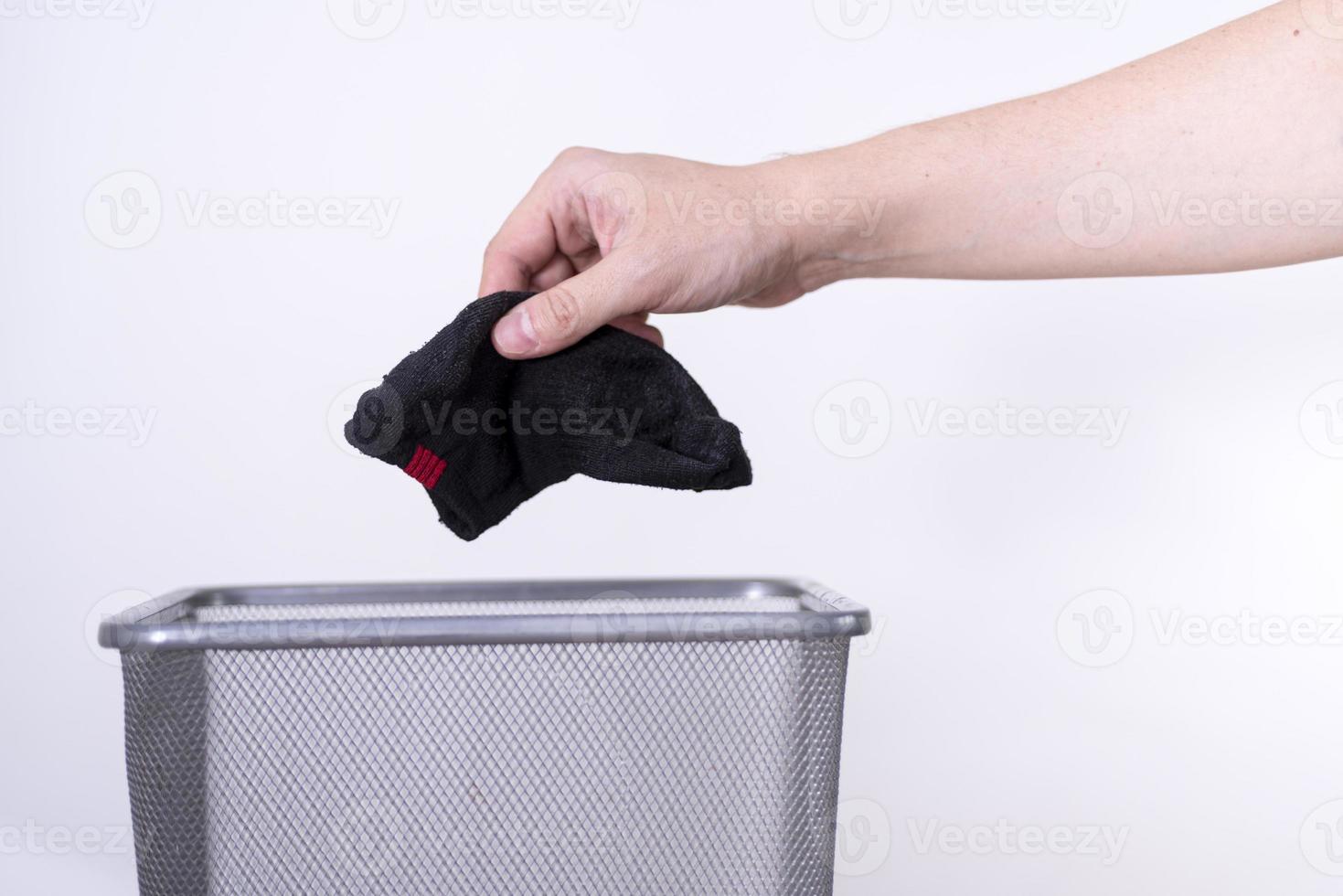 um homem está jogando uma meia velha em uma lata de lixo com a mão contra um fundo branco. foto