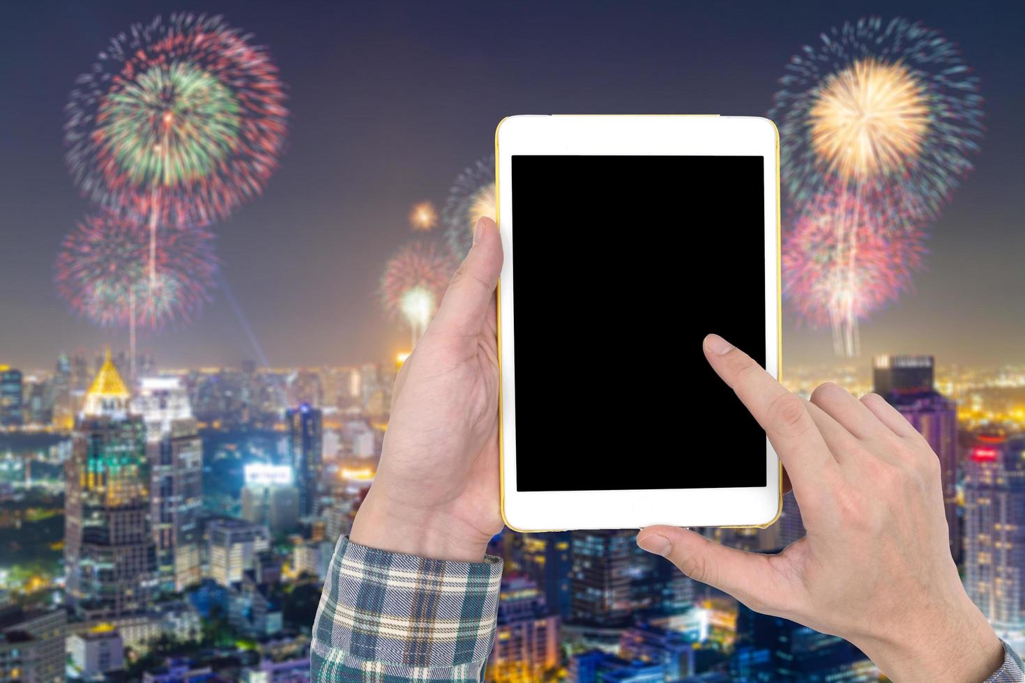 mão masculina segurando um gadget de computador tablet touch com tela de toque em branco na paisagem da cidade turva e fundo de fogos de artifício. foto