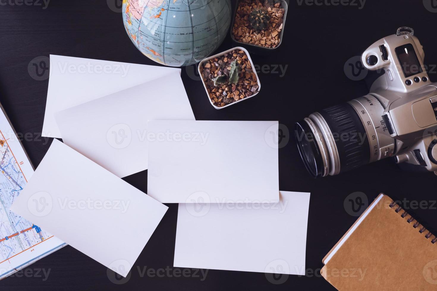 vista superior de cartões fotográficos em branco com câmera, cacto, mapa, globo e notebook na mesa do escritório. foto