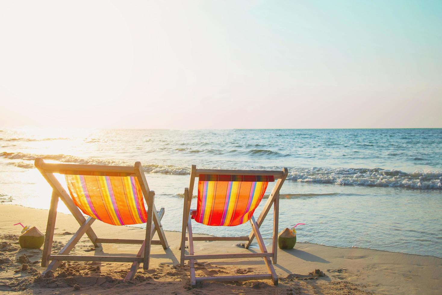 casal relaxa cadeira na praia de areia com pôr do sol quente - férias no belo conceito de natureza do mar foto