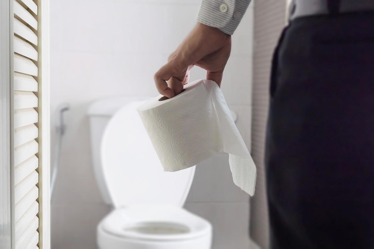 homem sentado no vaso sanitário segurando papel de seda - conceito de problema de saúde foto