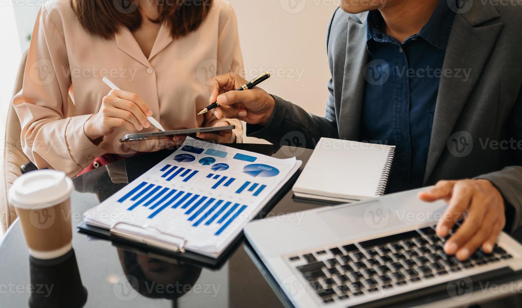 mão de empresário usando laptop e tablet com diagrama de rede social e dois colegas discutindo dados na mesa como conceito foto