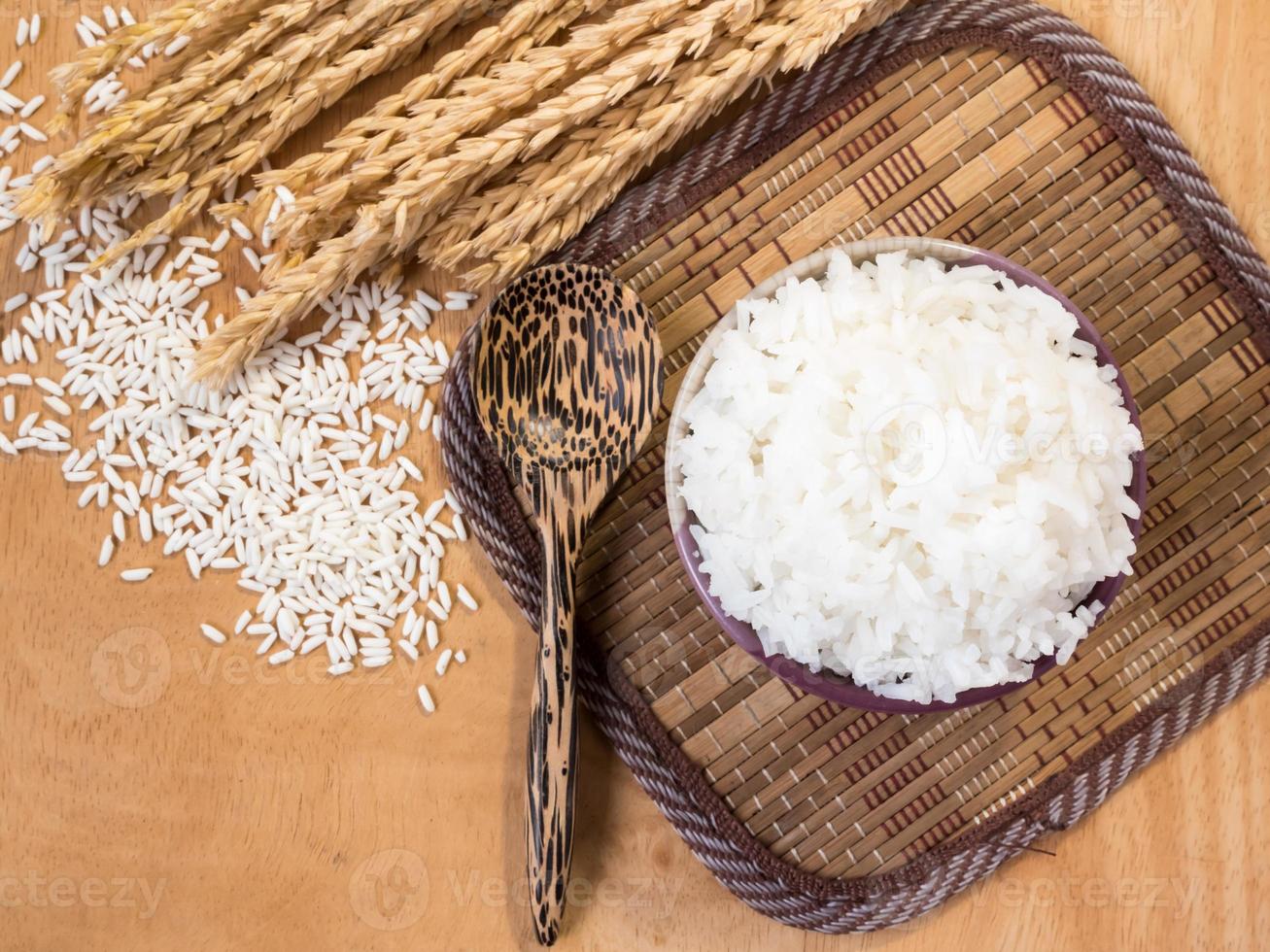 arroz cozido em tigela com grão de arroz cru e planta de arroz seco no fundo da mesa de madeira. foto