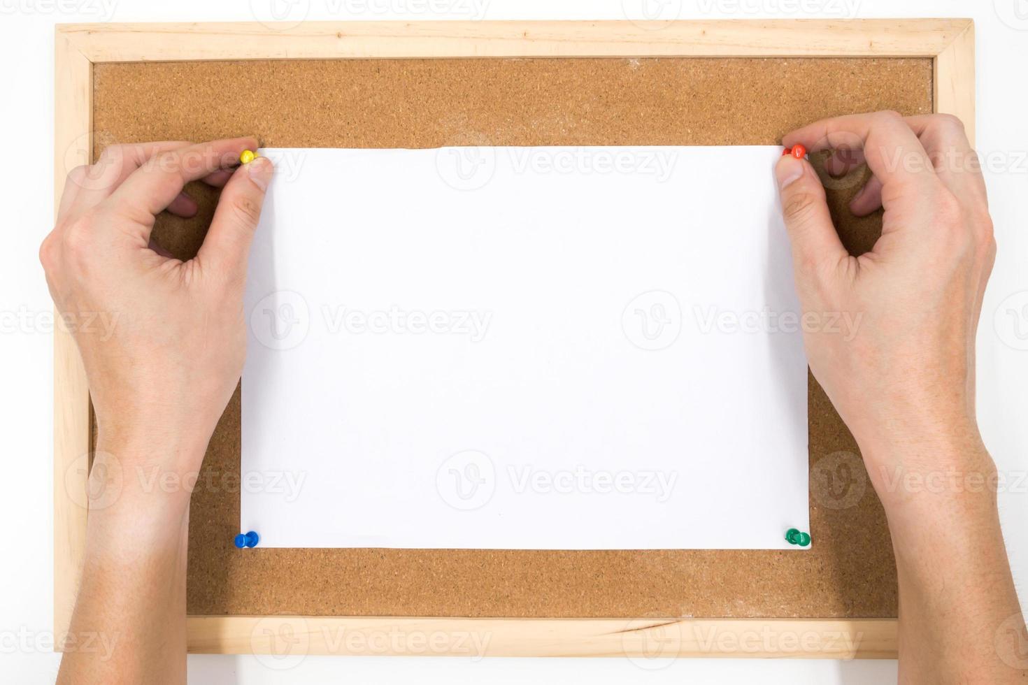 pino de papel em branco com as mãos na placa de cortiça. foto
