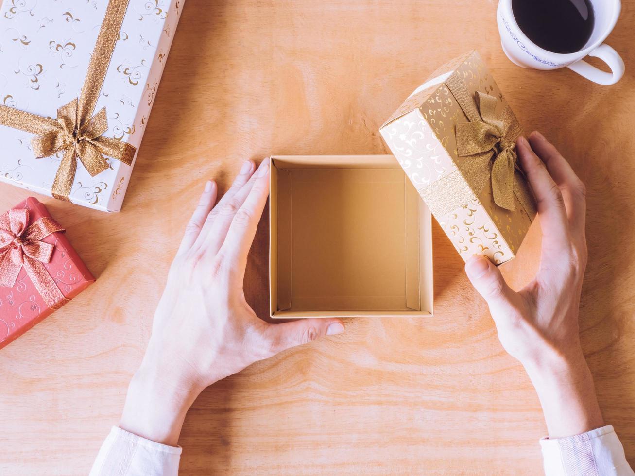 vista superior das mãos masculinas abrindo a caixa de presente, xícara de café na mesa de madeira. foto