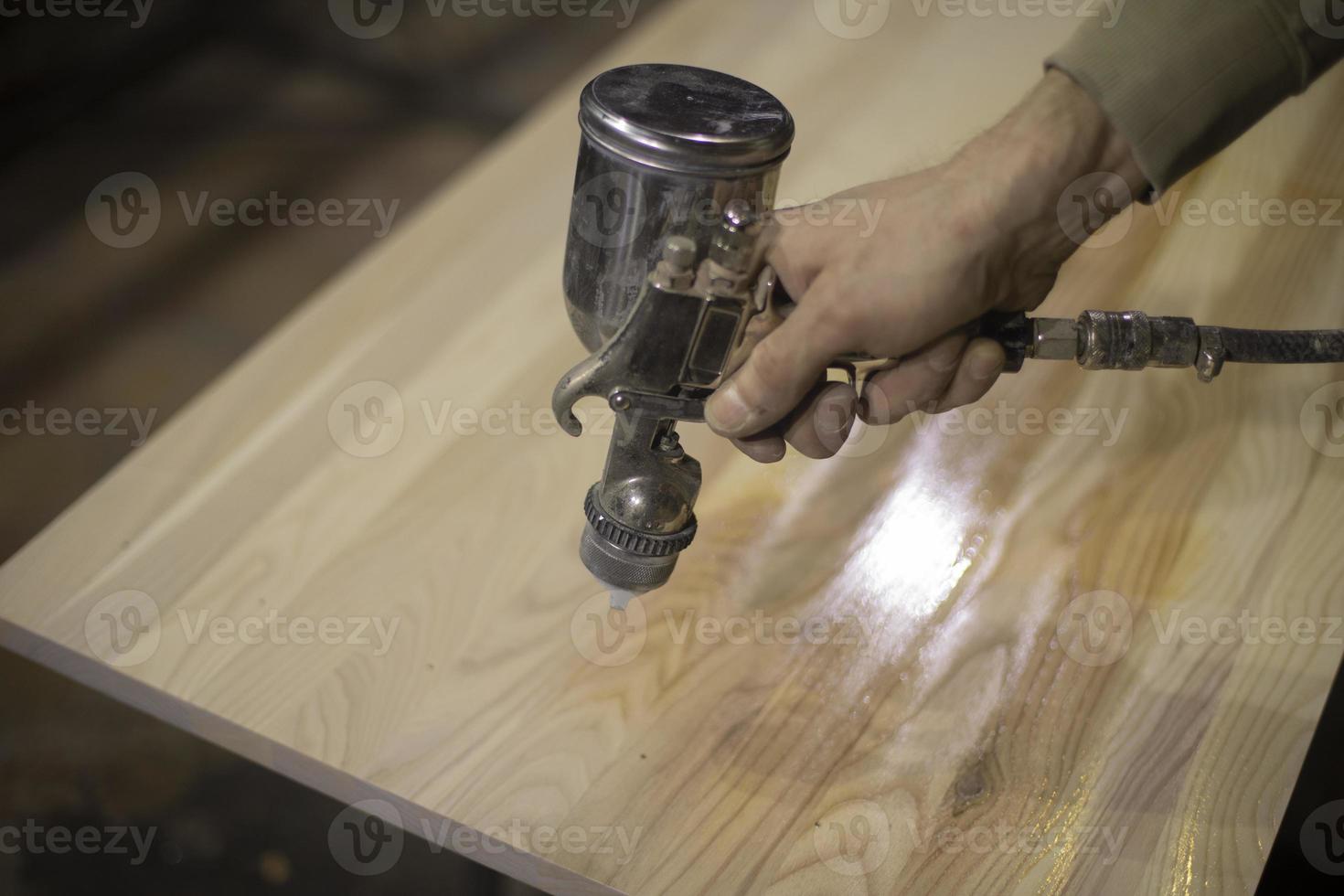 aplicação de verniz na placa. pistola de pintura para fornecimento de tinta. instrumento está na mão do homem. processamento de madeira. foto