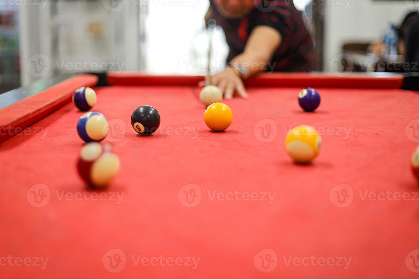 close-up da mão de um homem jogando bilhar se preparando para atirar a bola branca para a bola amarela com um conjunto completo de bolas de bilhar foto