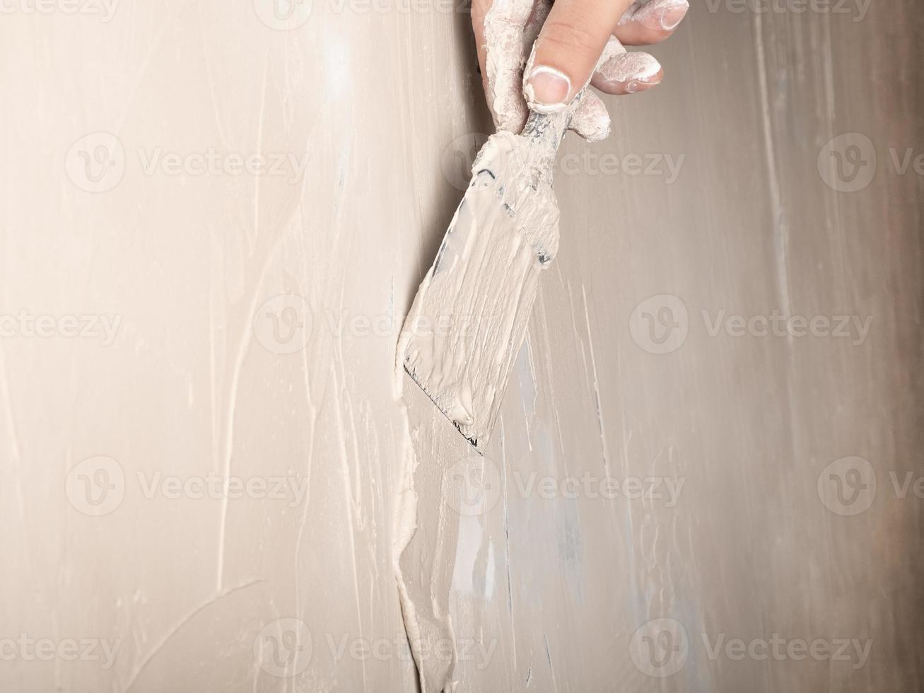 aplicação manual de massa de parede com uma espátula closeup, trabalho de reparo de gesso foto