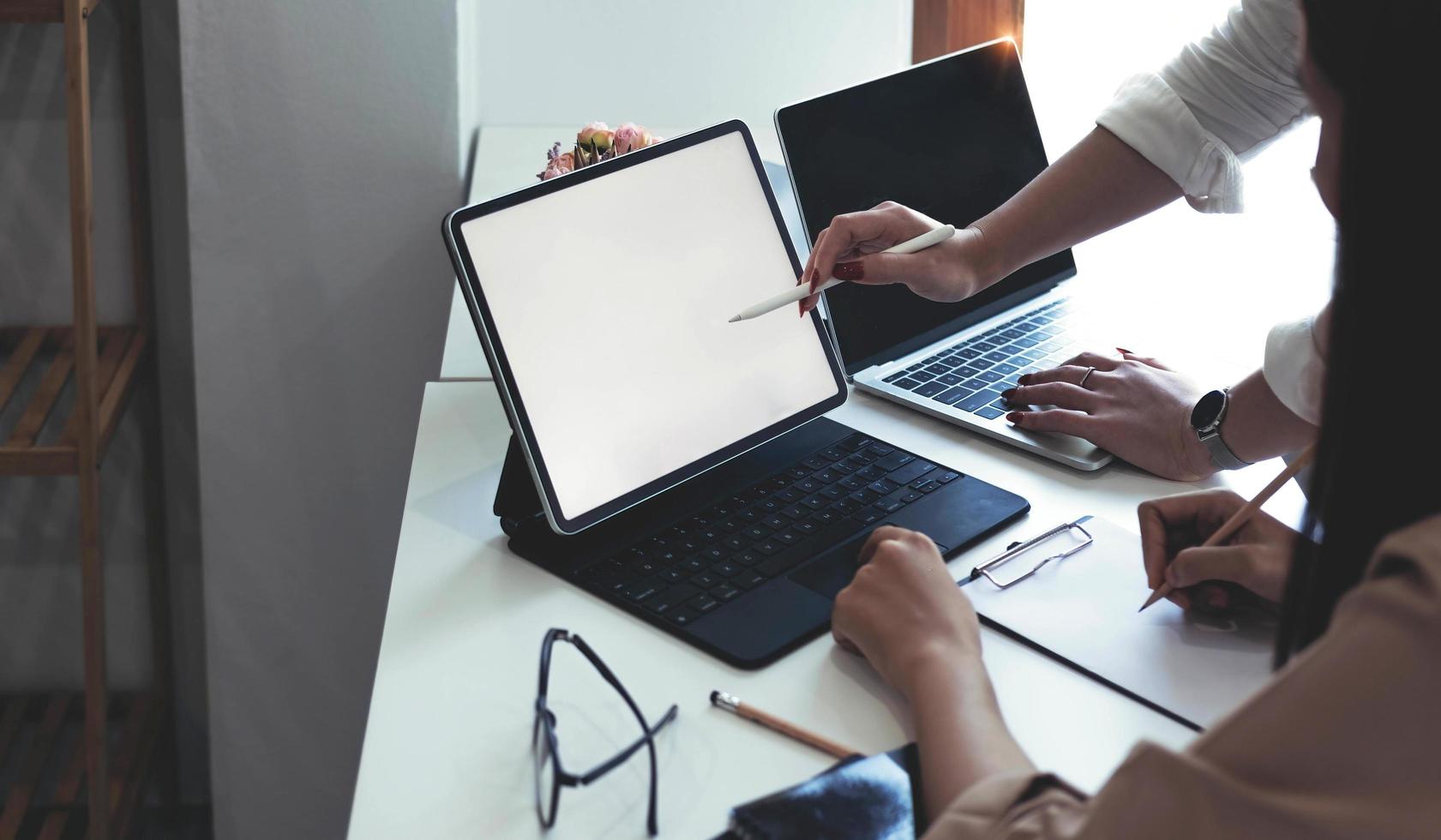 duas empresárias se encontram em uma sala de reuniões para uma consulta de negócios, usando um laptop e um tablet. maquete de um laptop com uma tela em branco foto