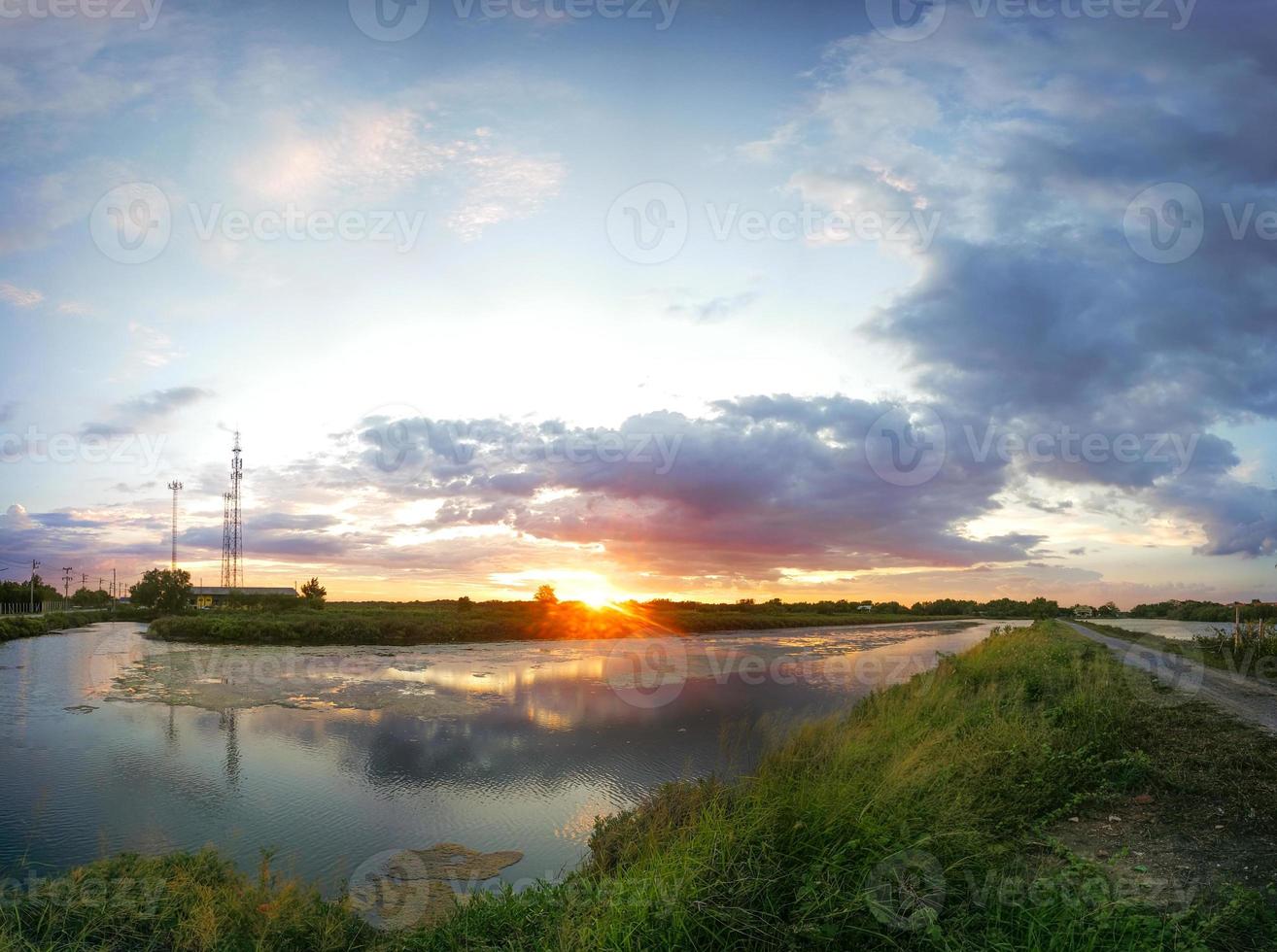 a lagoa reflete a luz do sol laranja. a borda da piscina é grama verde e amarela. o céu noturno antes do pôr do sol é colorido. foto