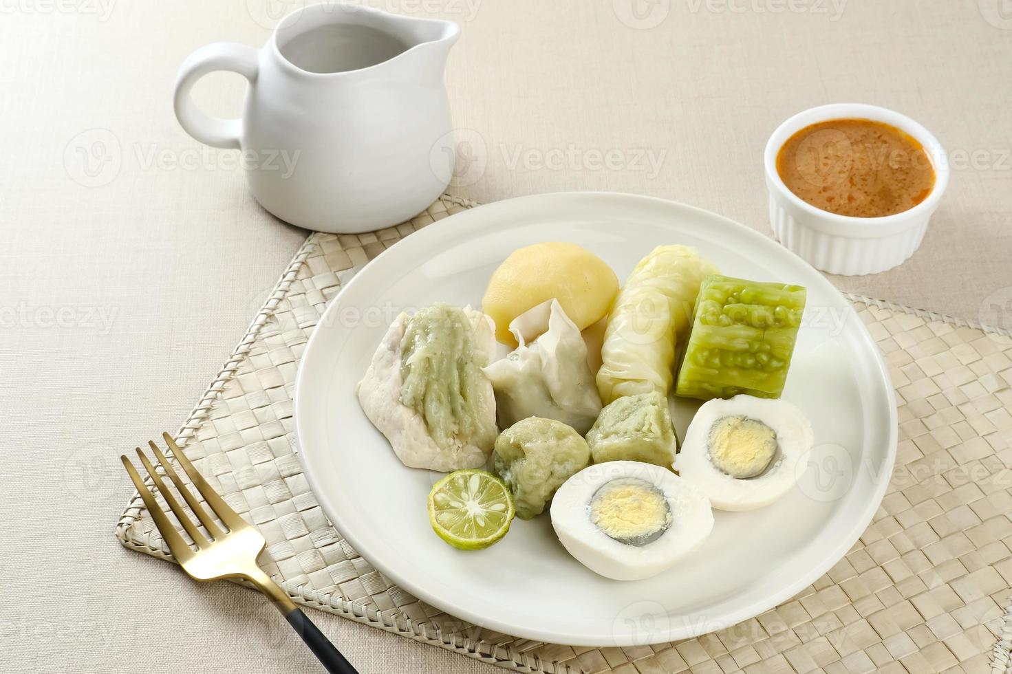 siomay bandung, bolinhos cozidos no vapor com ovo cozido, tofu, batatas e rolo de repolho. comida de rua tradicional indonésia com molho de amendoim e molho de soja, servido com limão verde. foto