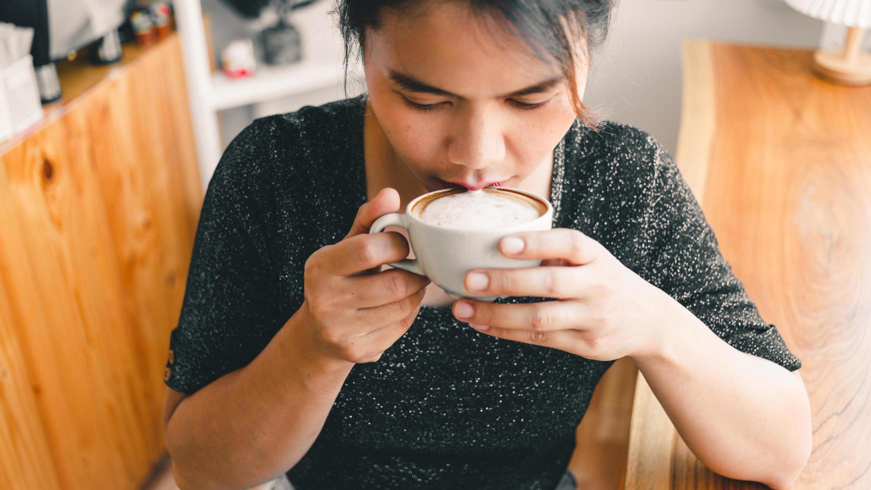 closeup de uma linda garota cheirando e bebendo café quente com se sentindo bem no café ela gosta de seu cappuccino matinal com café com espuma de leite foto