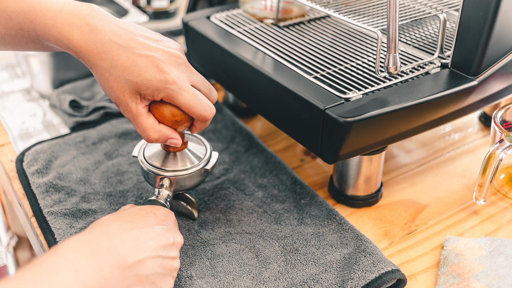 o barista prensa o café moído usando um calcador em um balcão de madeira com uma máquina de café automática colocada na cafeteria. foto