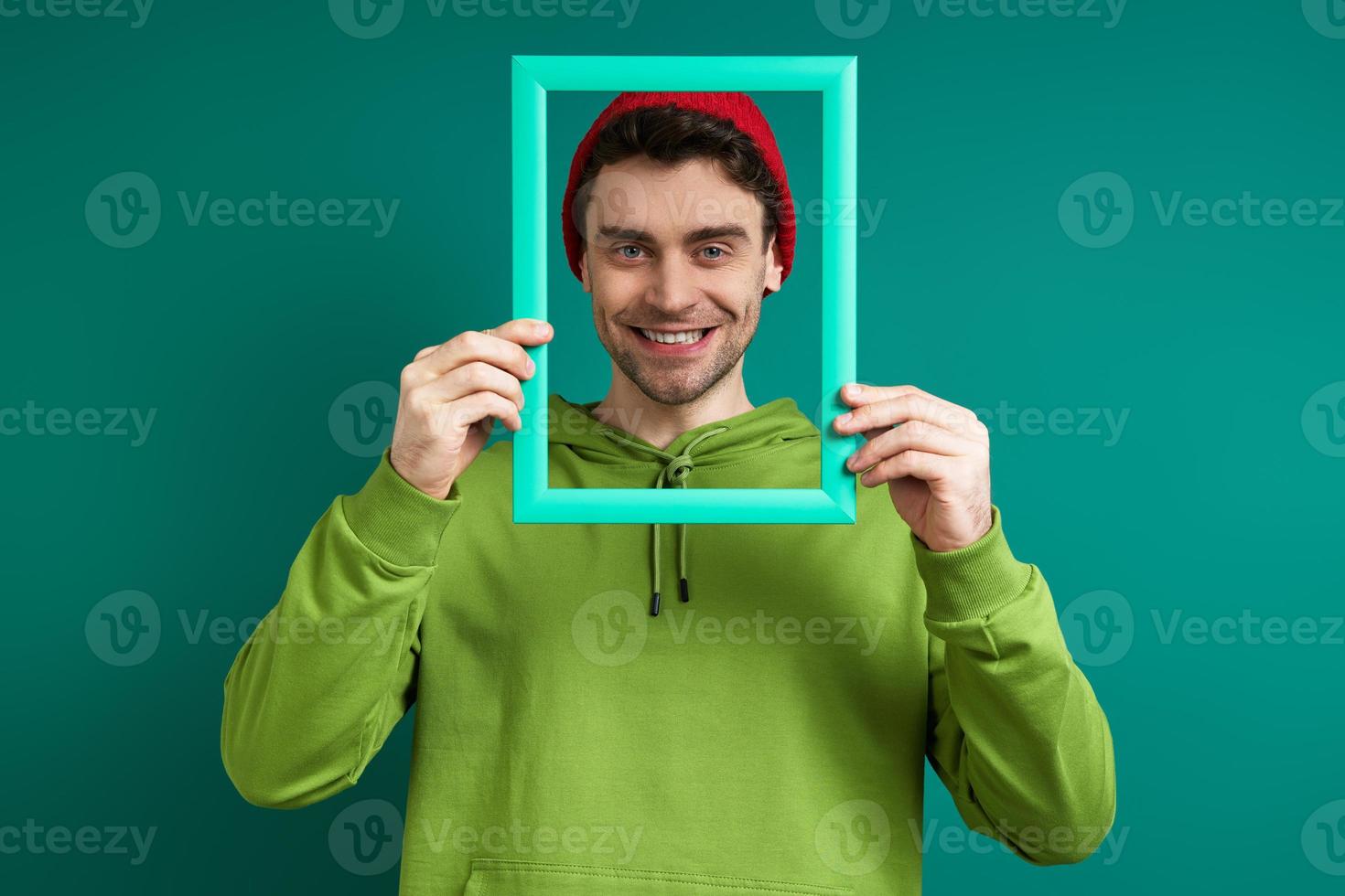 homem bonito olhando através de um porta-retrato e sorrindo em pé contra um fundo verde foto