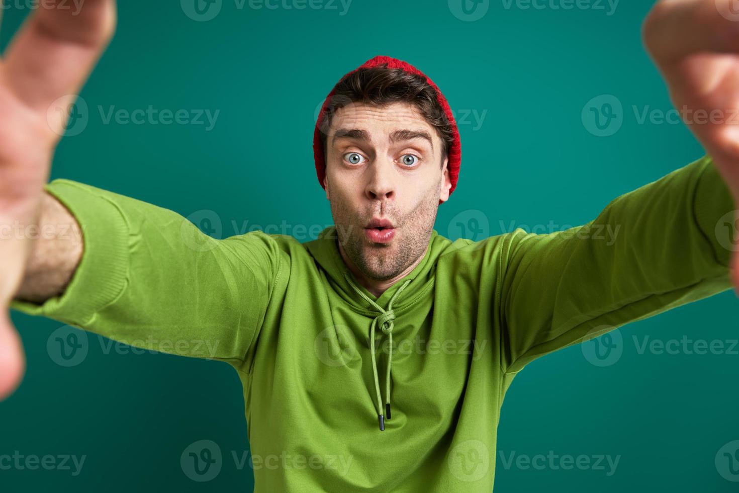 jovem surpreso olhando através de uma moldura de dedo em pé contra um fundo verde foto