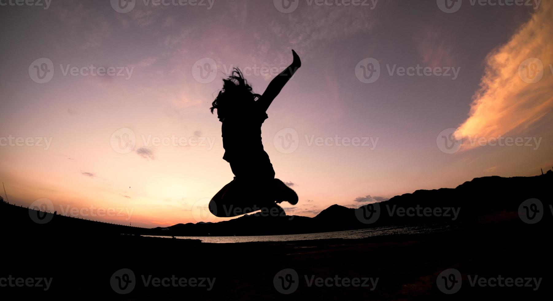 silhueta, garota de sombra pulando feliz pula no céu laranja à noite foto