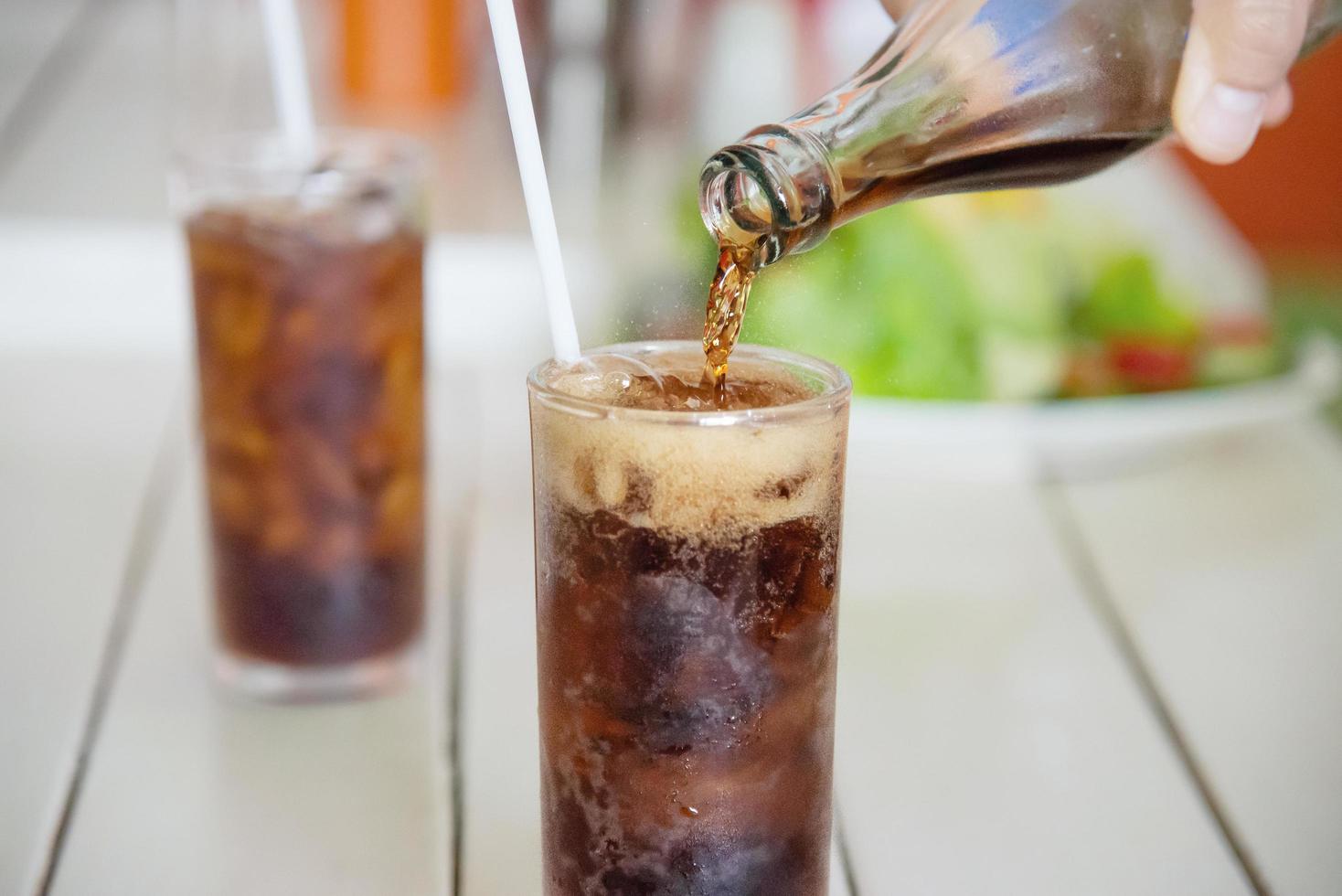 mão despeje refrigerante em um copo com gelo - conceito de bebida gelada refresco com sede foto