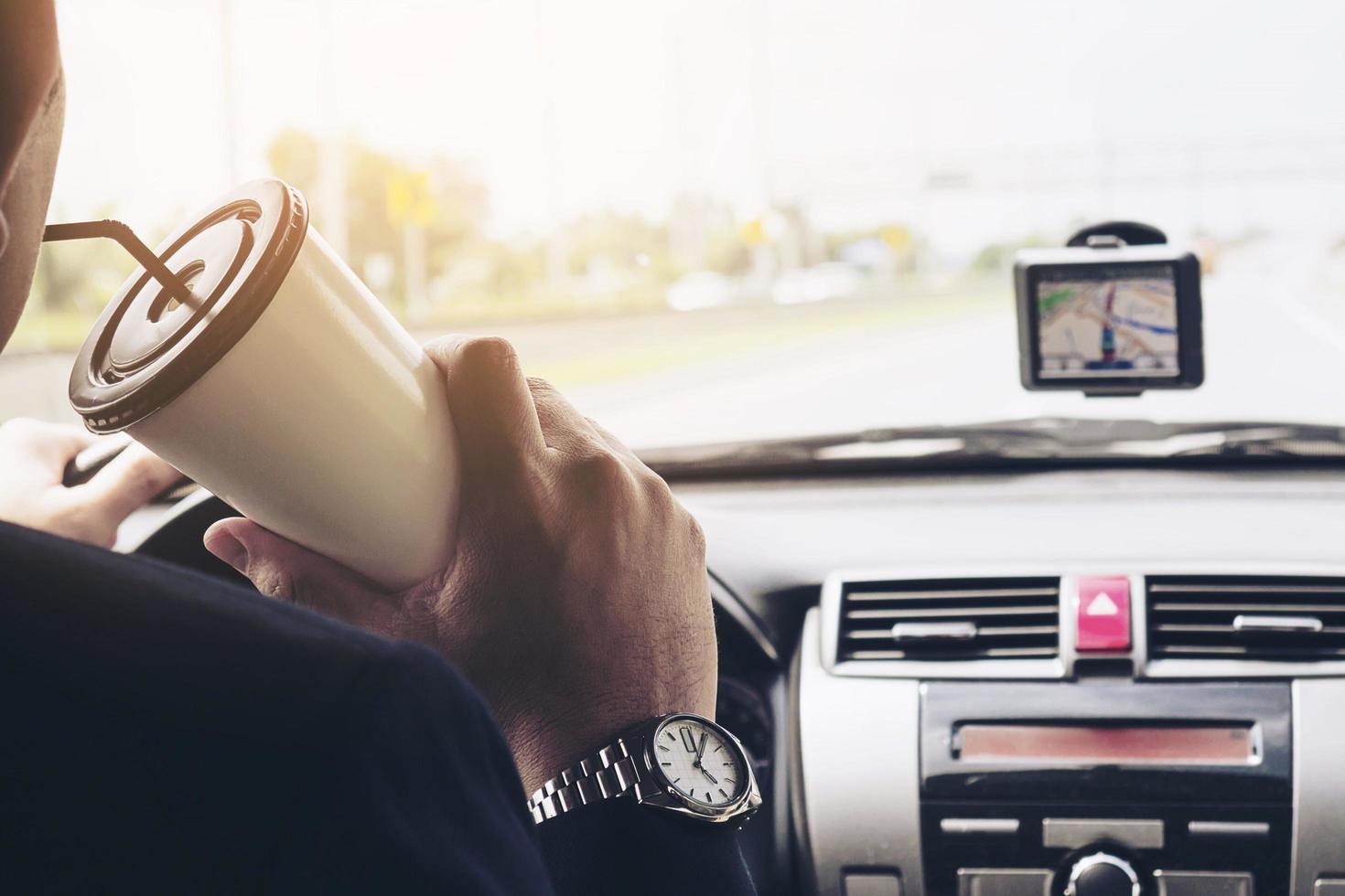 homem dirigindo carro usando navegador e segurando a xícara de café foto