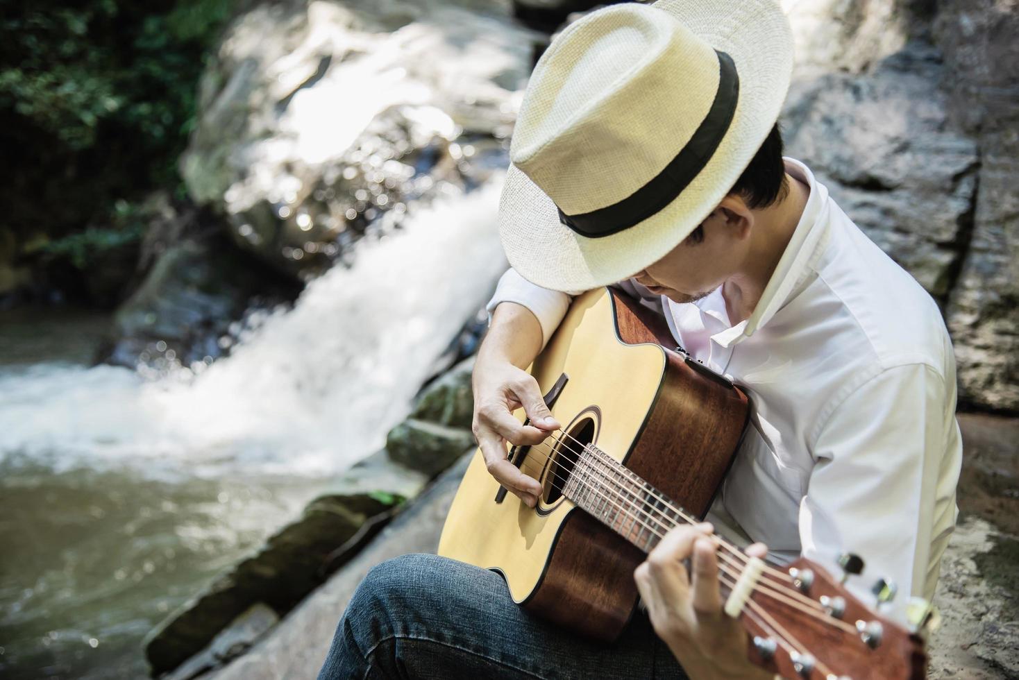 homem toca guitarra perto da cachoeira - estilo de vida de pessoas e instrumentos musicais no conceito de natureza foto