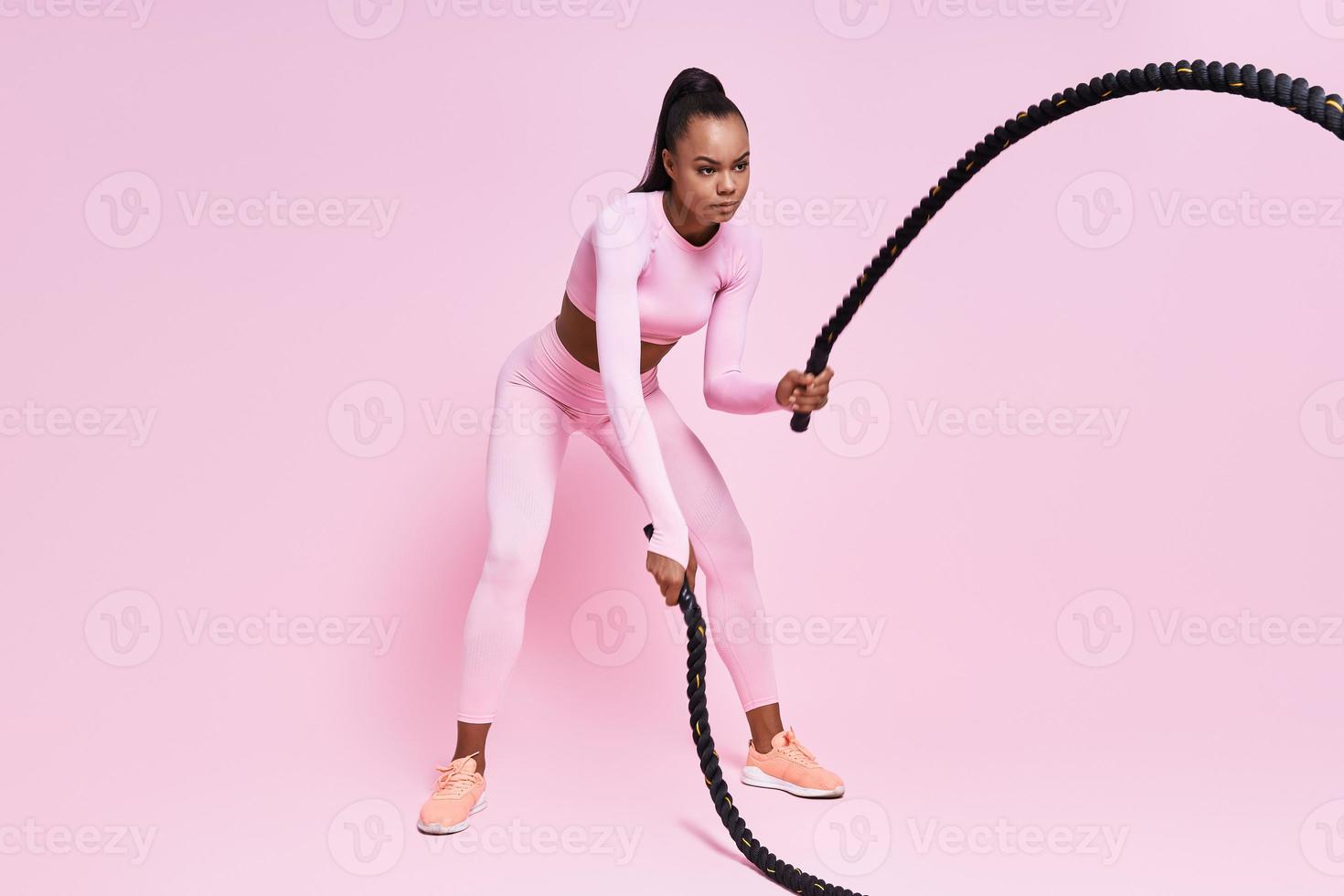 concentrada jovem africana exercitando com cordas de batalha contra fundo rosa foto