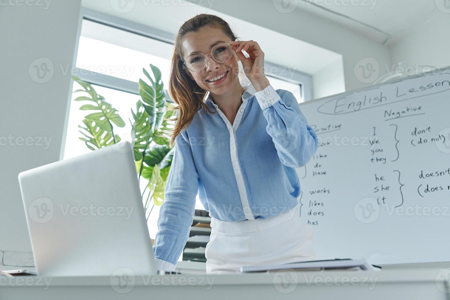 jovem feliz usando laptop em pé perto do quadro branco na sala de aula foto