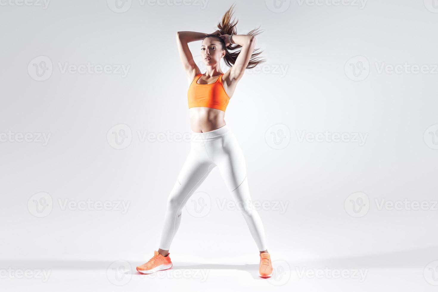 mulher jovem e bonita em roupas esportivas, ajustando o cabelo contra o fundo branco foto