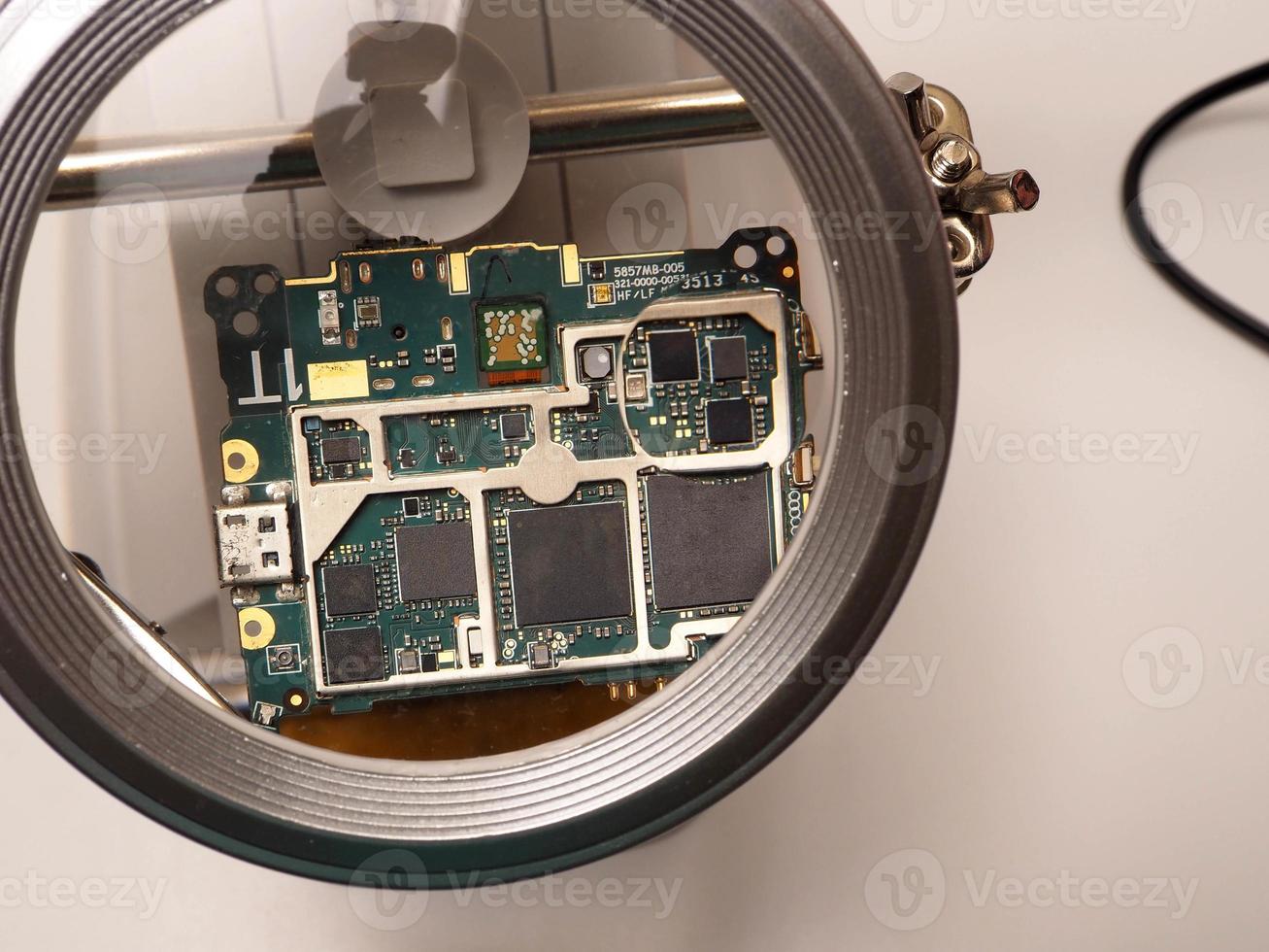close-up tiro de placa de circuito impresso pcb sentado em um suporte de reparo branco com lupa para melhor examinar peças pequenas foto