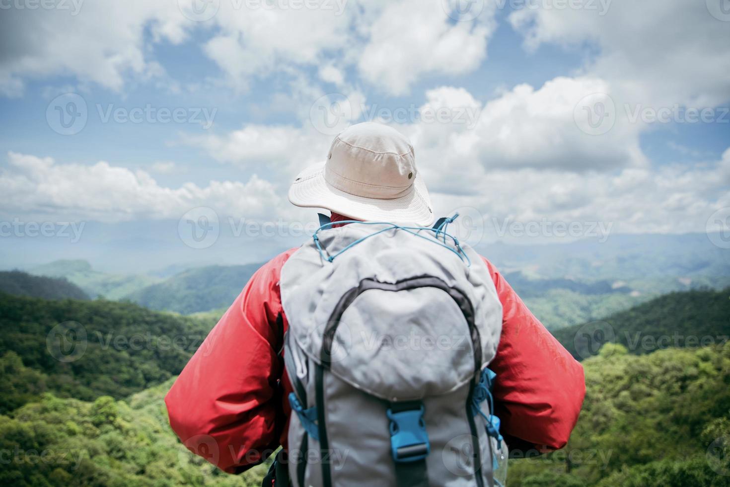 jovem caminhadas masculinas no topo da rocha, mochila homem olhando para o belo vale da montanha à luz do sol no verão, paisagem com esporte homem, altas colinas, floresta, céu. viagem e Turismo. foto