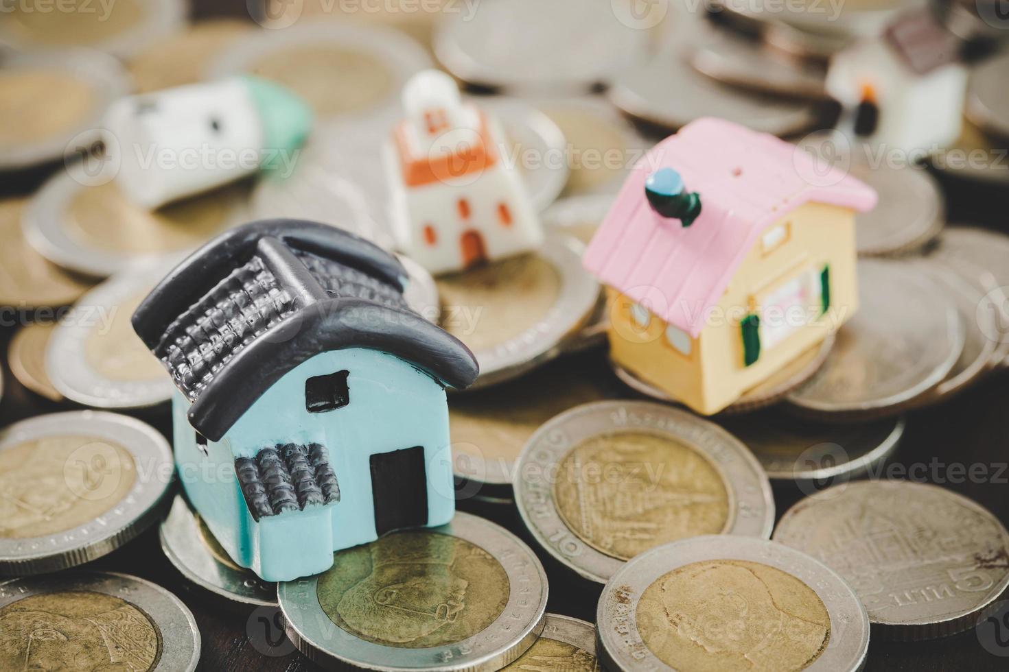 modelo de casa e pilhas de moedas de dinheiro no fundo da mesa desfocada. planos de poupança para casa, empréstimo, investimento, hipoteca, finanças e serviços bancários sobre o conceito de casa. foto