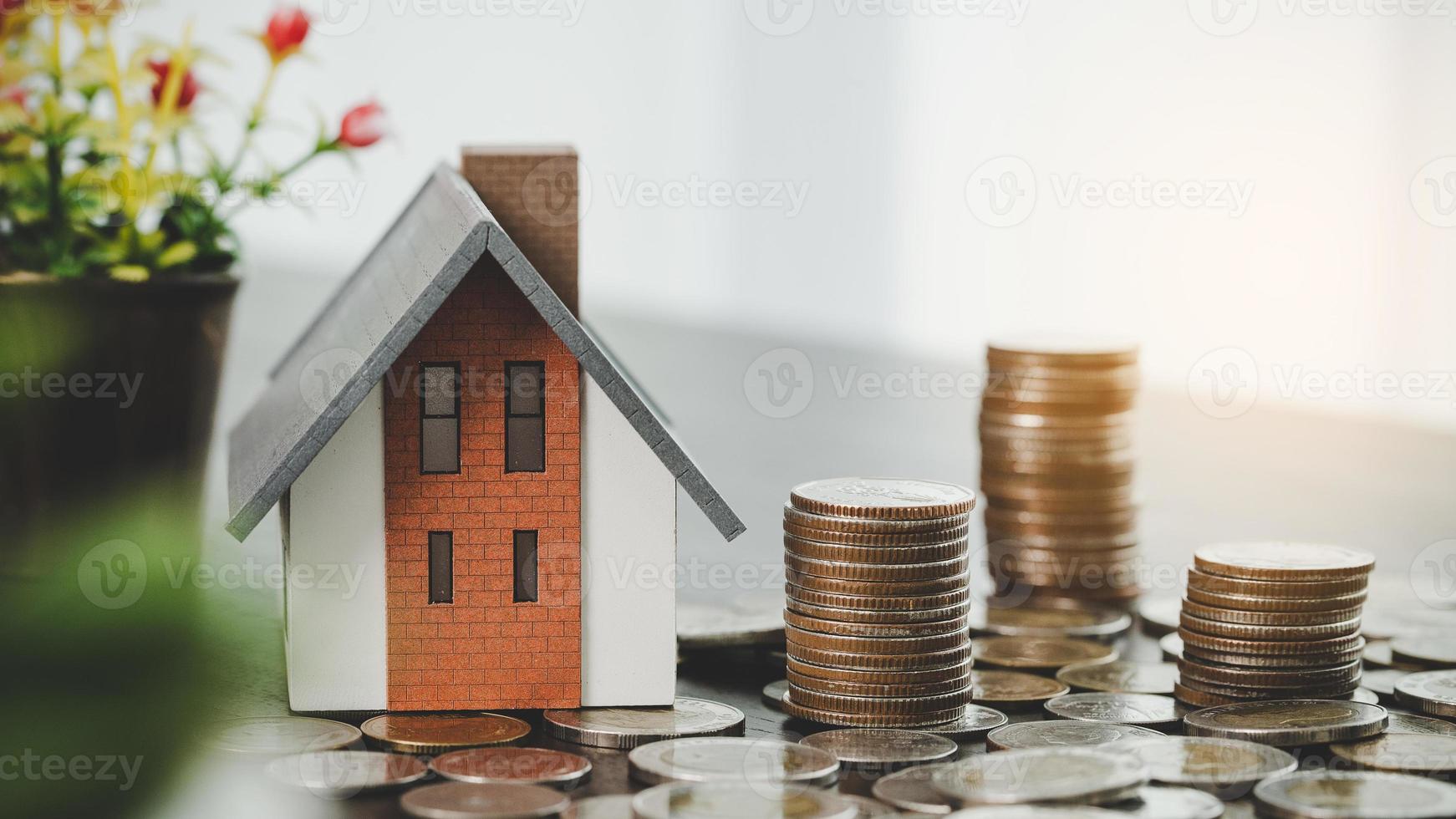 modelo de casa e pilhas de moedas de dinheiro no fundo da mesa desfocada. planos de poupança para casa, empréstimo, investimento, hipoteca, finanças e serviços bancários sobre o conceito de casa. foto