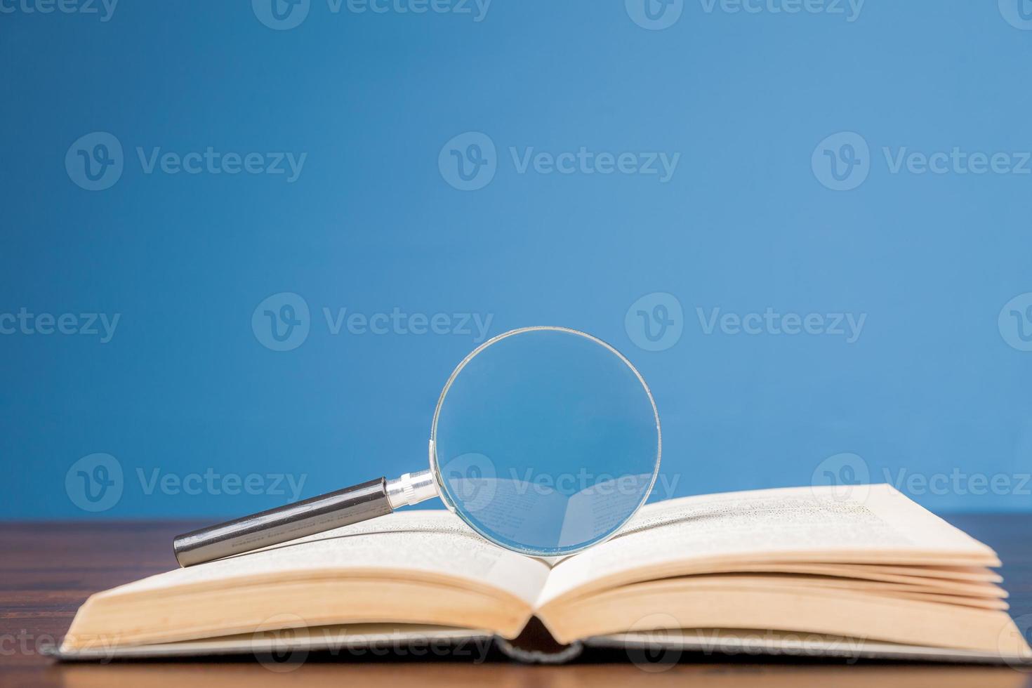 livro aberto com lupa na mesa de madeira na biblioteca de informações da escola ou universidade, conceito para educação, leitura, estudo, espaço de cópia e fundo azul. foto