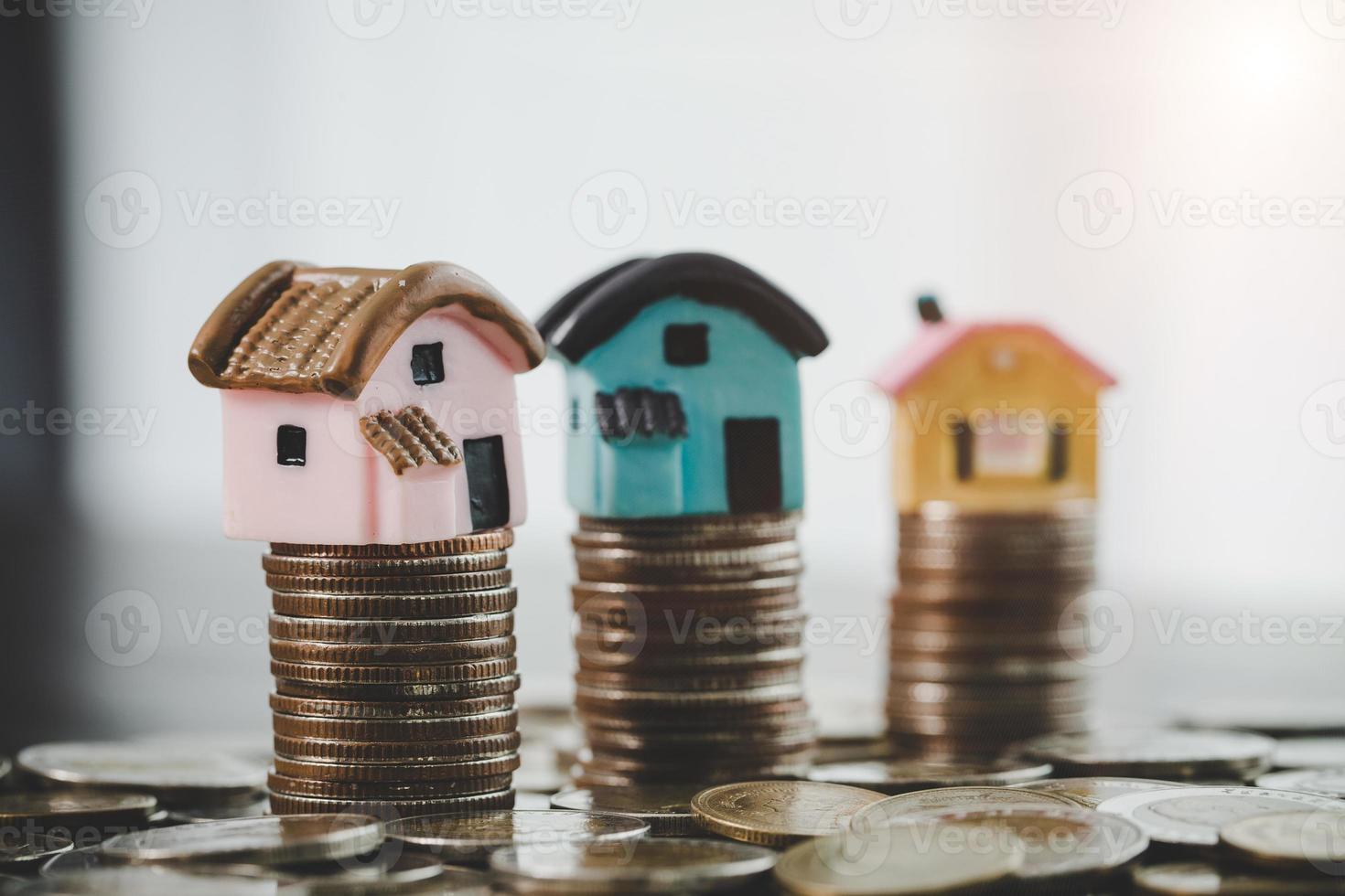 modelo de casa e pilhas de moedas de dinheiro no fundo da mesa desfocada. planos de poupança para casa, empréstimo, investimento, hipoteca, finanças e serviços bancários sobre o conceito de casa. foto