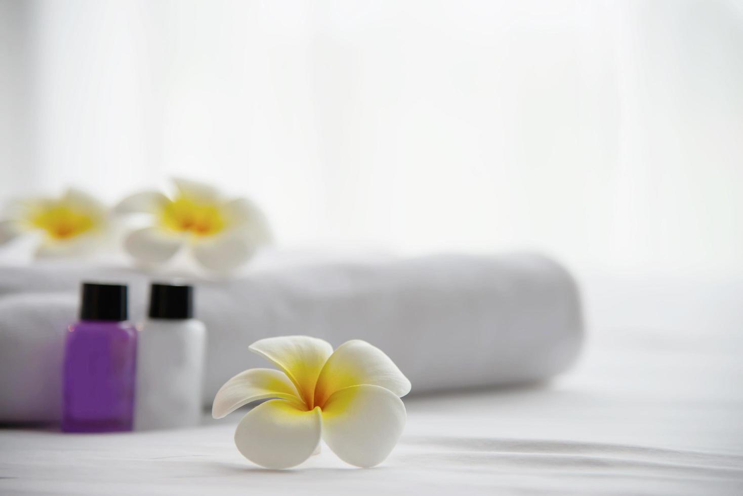 toalha de hotel e garrafa de banho de shampoo e sabonete em cama branca com flor de plumeria decorada - relaxe as férias no conceito de resort de hotel foto